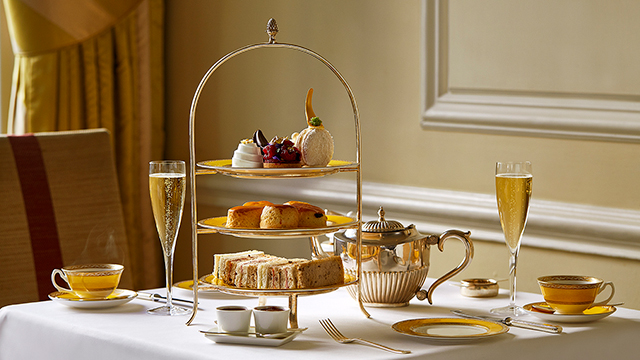 An afternoon tea, laid out on a three-tiered cake stand, with two glasses of champagne, teacups and a teapot.