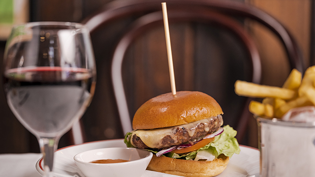 Close up on a cheeseburger and its fries accompanied for a glass of red wine at the American brasserie Joe Allen in Covent Garden.