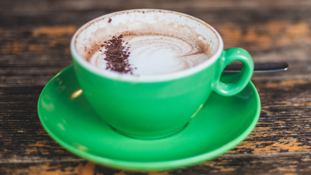 A frothy cup of coffee in a green cup and saucer