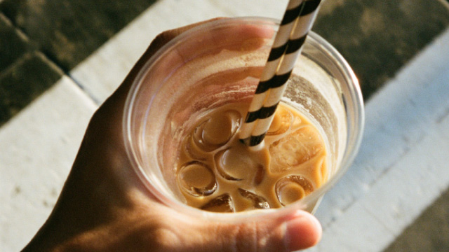 A person holding a glass of iced coffee with two striped straws