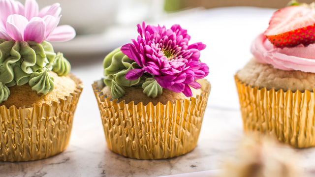 Three colourful cupcakes covered in icing, fruit and flowers
