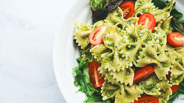 A plate of pasta bows with pesto, green leaves and red tomatoes
