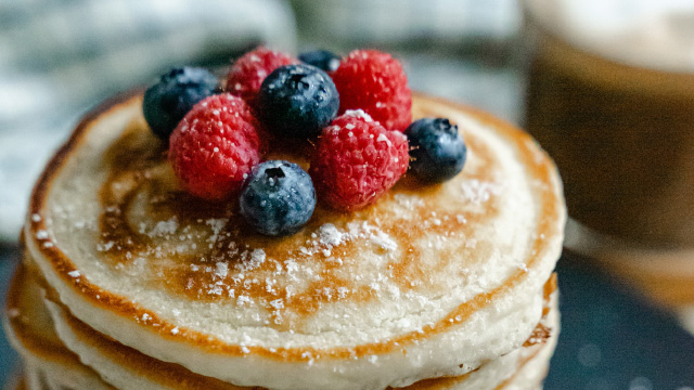 A stack of pancakes topped with raspberries, blueberries and sugar icing 