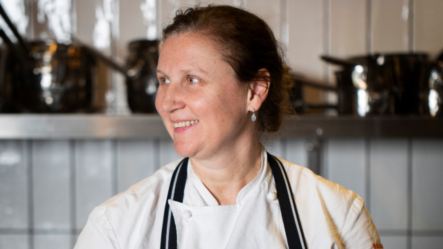 Meet Angela Hartnett, the chef behind Murano in Mayfair and Cafe Murano. Image courtesy of Angela Hartnett Angela Hartnett is posing for the camera in a tiled kitchen, with pan and pots on shelves in the background.