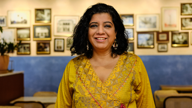 Meet Asma Khan, proprietor at Darjeeling Express and cookbook author. Image courtesy of Asma Khan Asma Khan is smiling and posing for a portrait in her restaurant.