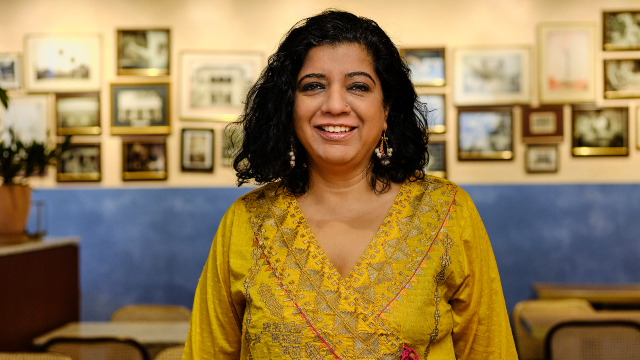 Asma Khan is smiling and posing for a portrait in her restaurant.
