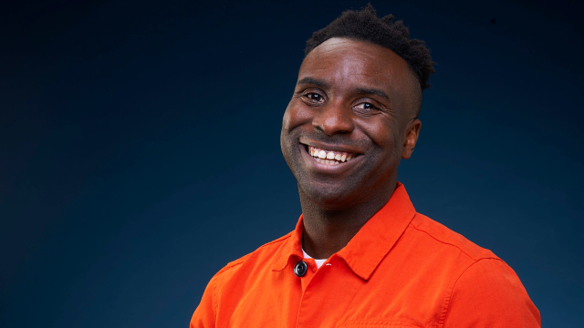 Meet journalist Jimi Famurewa. Credit Natasha Pszenicki for the Evening Standard Standing in front of a dark background, Jimi Famurewa is smiling and looking at the camera, wearing a bright shirt.