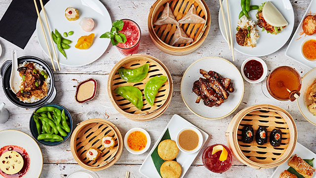 An overhead shot of steamed Dim Sum, bao, buns and gyozas on a table with plates and chopsticks