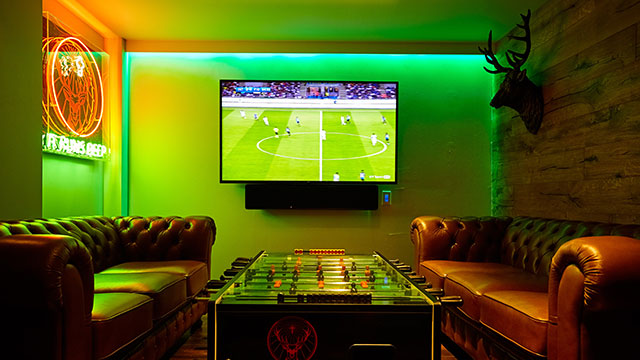 Two brown leather couches and a football table in front of a giant tv screen on a green wall