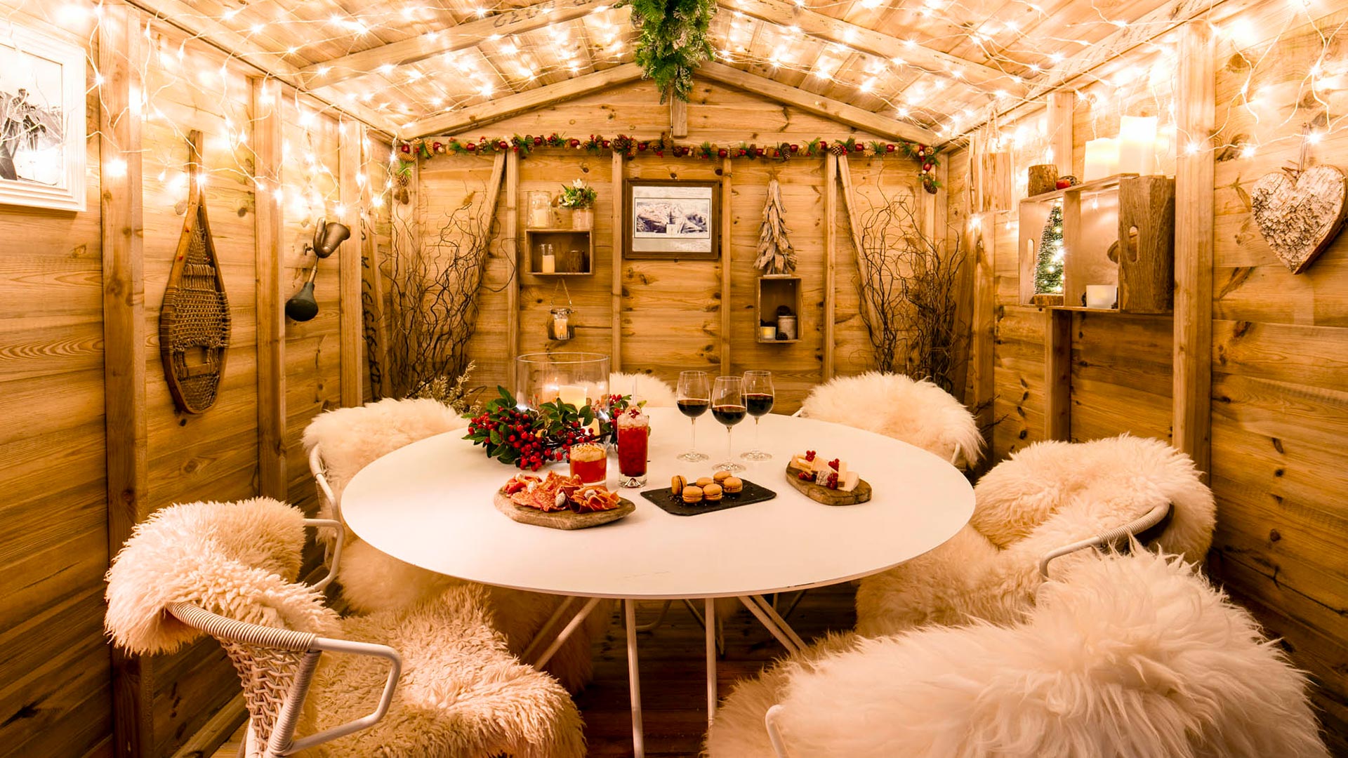 The inside of a wooden chalet at Lodge d'Argent, with fur-covered chairs, cocktails, drinks and small plates of food on a table, and lit fairy lights.