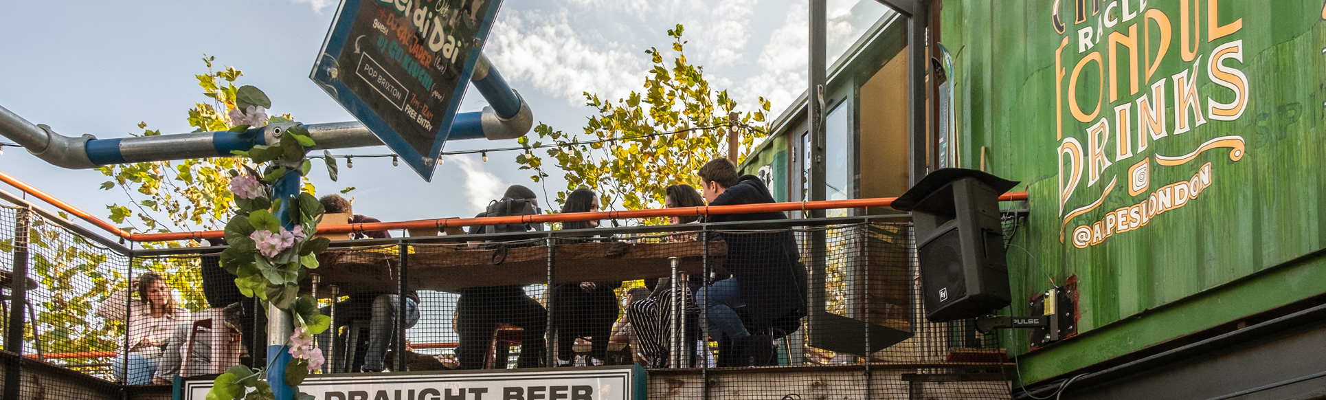 Summer at Pop Brixton. Credit: visitlondon.com/Gary Latham People sat on benches enjoying a drink in the sun on a roof terrace