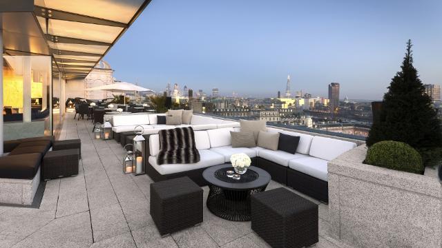 Eine menschenleere Terrasse mit Sitzgelegenheiten im Lounge-Stil und der Londoner Skyline im Hintergrund, in der Abenddämmerung.