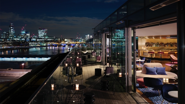 An outside rooftop bar terrace, overlooking the London skyline at night