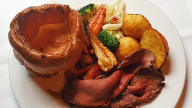 Close up of a Sunday roast featuring meat, potatoes, vegetables, a Yorkshire pudding and gravy.