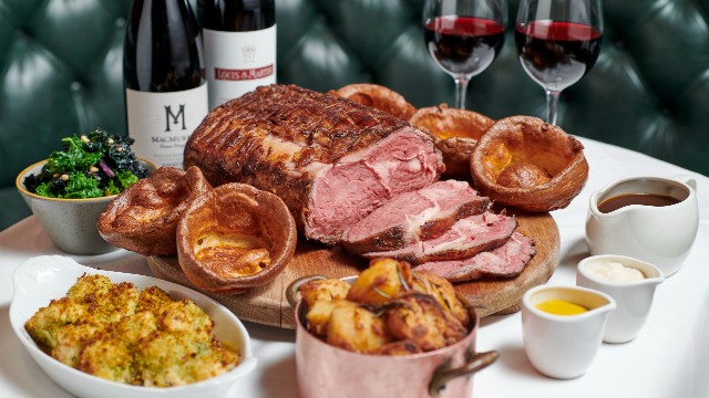 A Sunday roast feast laid out on a white-tablecloth table, featuring meat, vegetables, salad and wine.