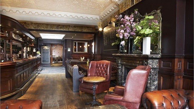 The interior of The White Horse, with a traditional bar on the left, wood flooring, and red leather armchairs on the right.