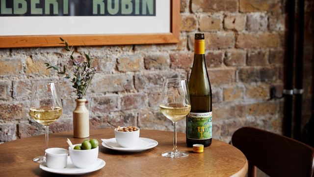 A brown table against a brick wall with bar snacks and glasses of white wine.