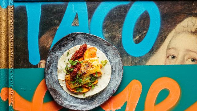Tacos plate viewed from above on colourful painted table featuring the word taco in blue.
