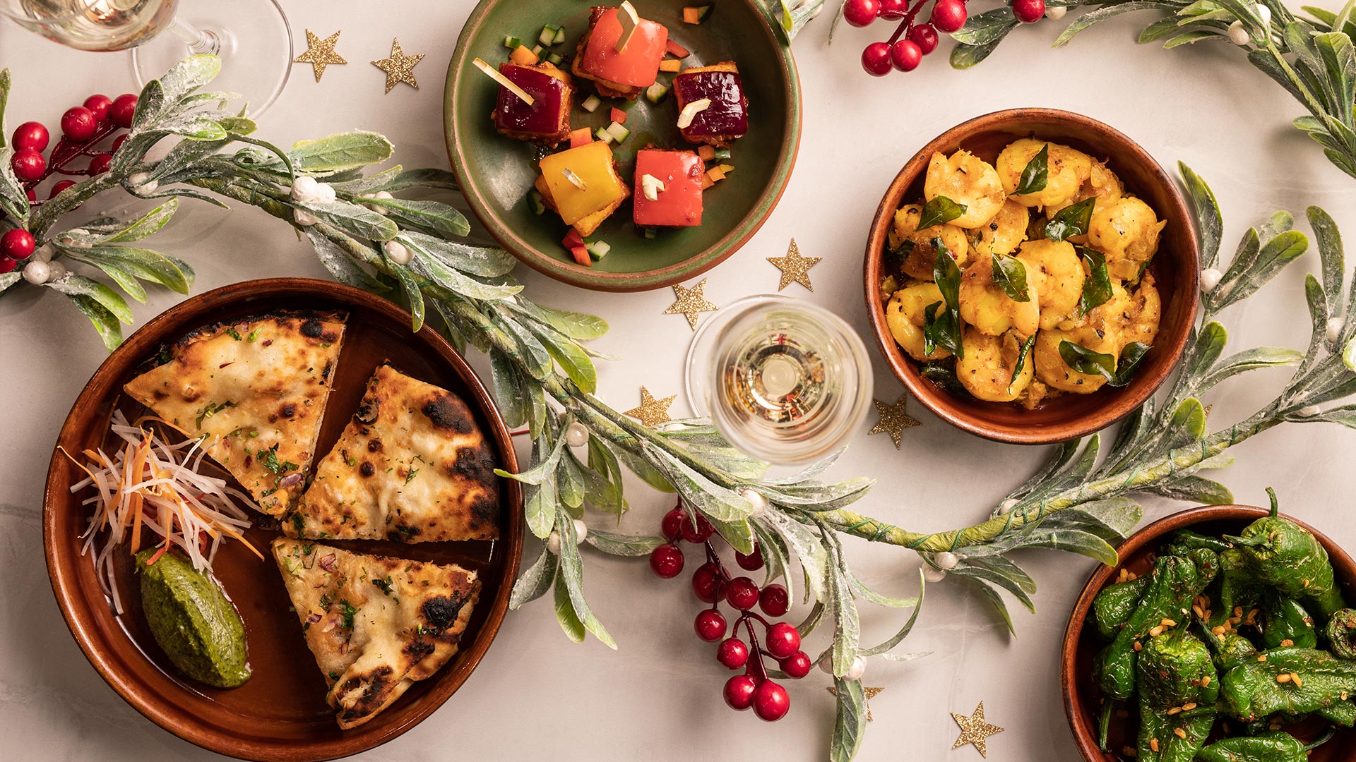 Four plates of food from the festive menu at Cinnamon Kitchen City sit on a table decorated with frosted foliage and stars.
