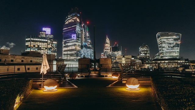 Rooftop bar at night time with a backdrop of the City of London in lights