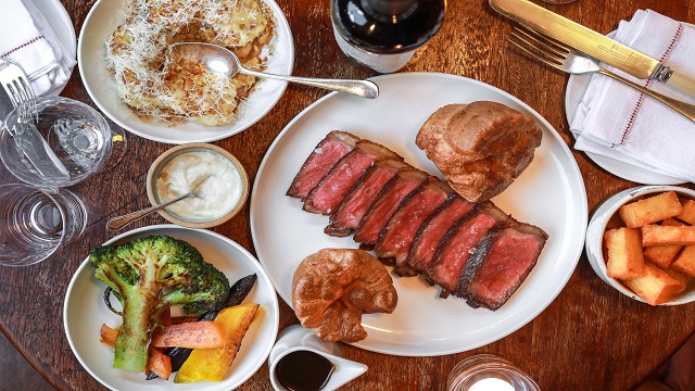 Plate of medium-rare roast beef and yorkshire puddings, surrounded by mini plates of vegetables and condiments