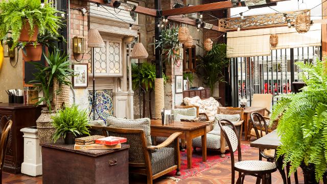 The dining area at Dishoom Shoreditch with hanging plants, cosy sofas and a tiled floor.