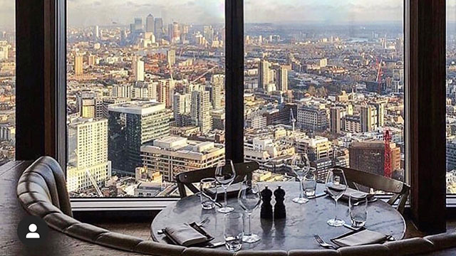 A dining table in front of a full length window with views of London on a sunny day