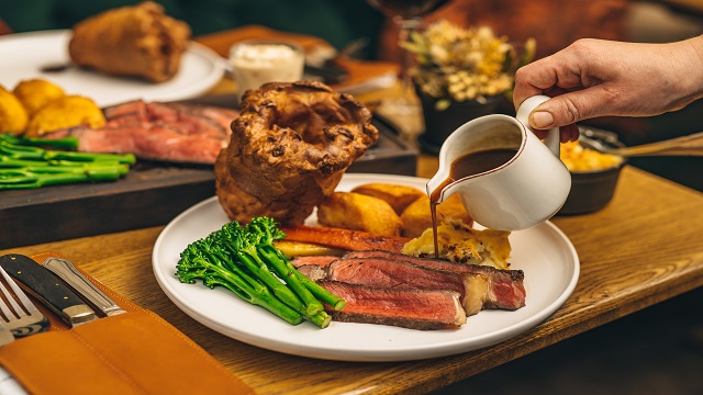 A table spread of roast dinners, with gravy being poured onto the plan in a small white jug