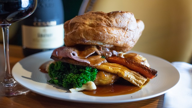 Roast dinner served on a plate in layers, starting with vegetables, meat and then topped with a big yorkshire pudding