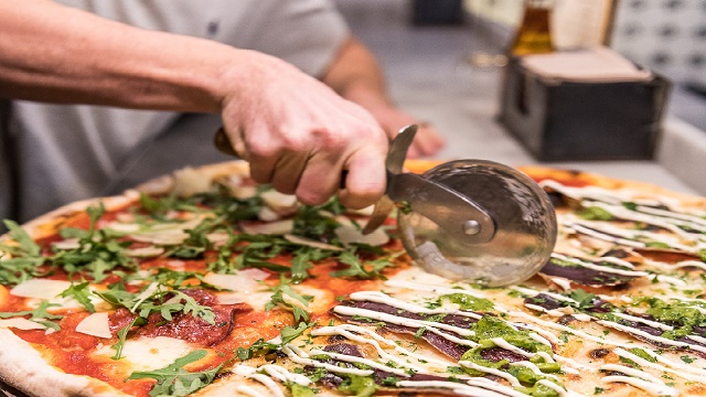 A large wagyu beef pizza being sliced with a pizza slicer