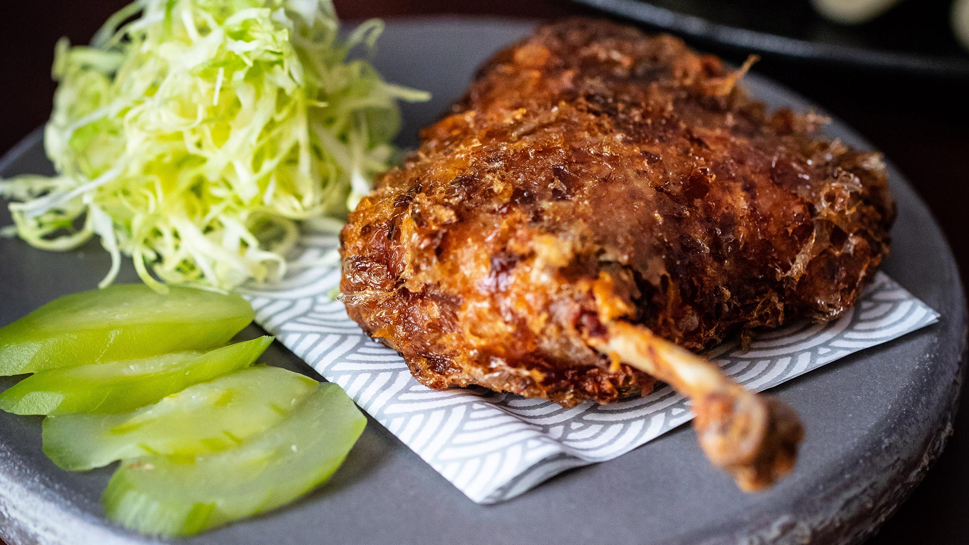 A leg of roast duck, four slices of cucumber and a ball of shredded spring onion sit on a plate at Lucky Cat by Gordon Ramsay.