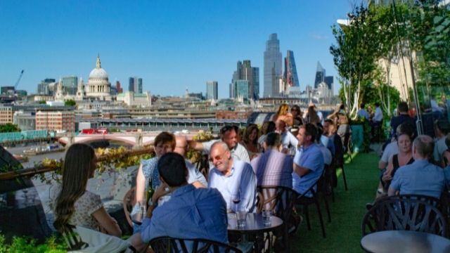 People enjoy food and drink on the OXO Tower rooftop with a view of the London skyline.