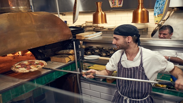 A chef putting a fresh pizza into the pizza oven