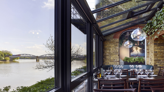 A landscape of a restaurant with big open windows overlooking the river