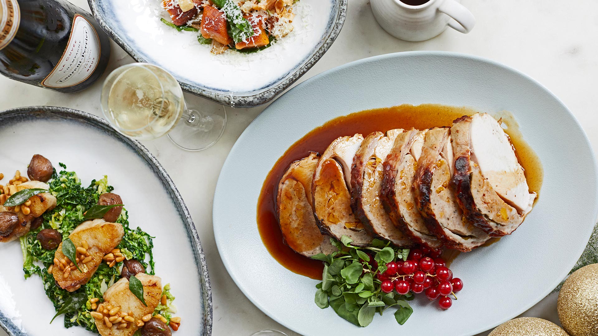 Sliced turkey breast sits on a plate with gravy and redcurrants, alongside two plates of vegetables and a glass and bottle of wine., at Sea Containers London.