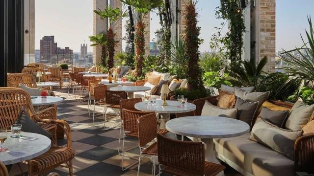 Rooftop terrace restaurant with chairs and tables set out or dining, with London skyline in distance.