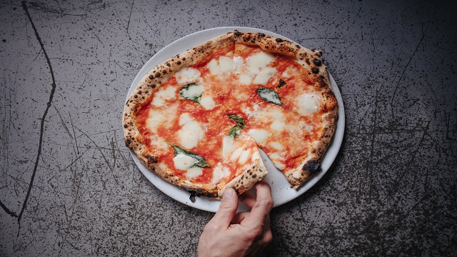 High angle shot of a large Margherita pizza, with a hand taking a slice