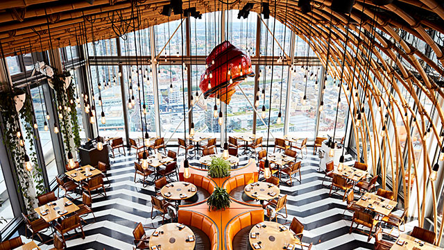 Sushisamba restaurant with orange tables, black and white floor, lights hanging from the ceiling and large windows with views of London.