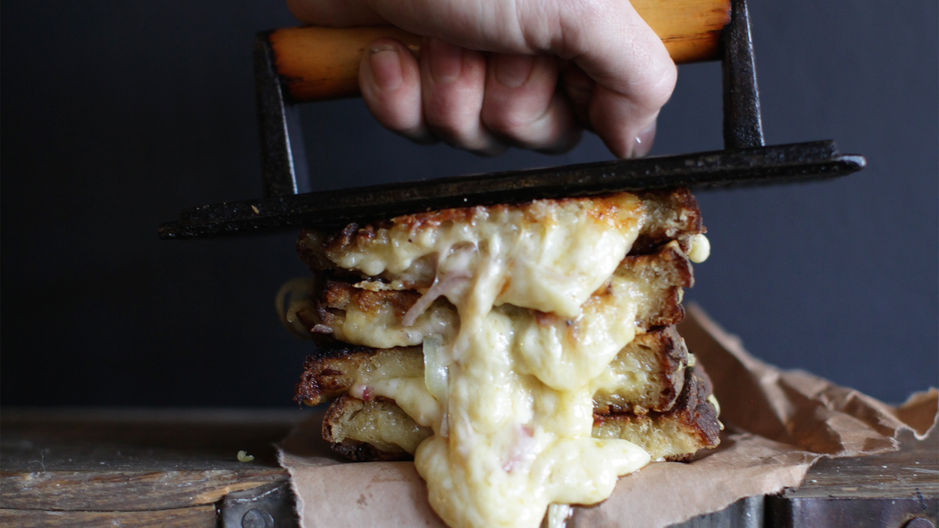 A toasted sandwich with cheese oozing out is squashed by The Cheese Truck's chef holding an iron press. Image courtesy of The Cheese Truck.