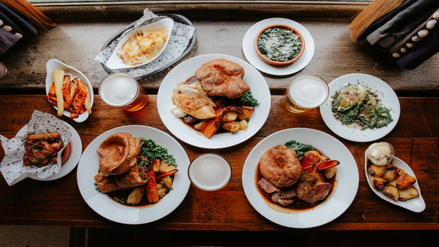 High angle shot of lots of plates of roast dinner on a wooden table, with side dishes surrounding the plates of roast dinners.