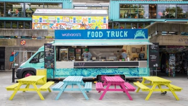 A brightly coloured Wahaca food truck with benches on London's South Bank. 