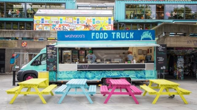 A brightly coloured Wahaca food truck with benches on London's South Bank.