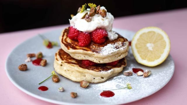 A plate of fluffy pancakes with whipped cream, raspberries and pistachios.