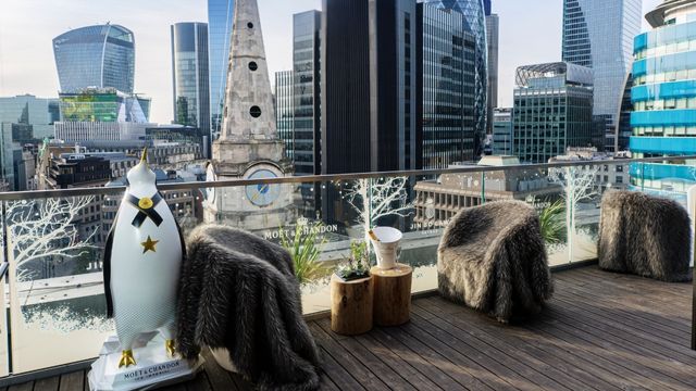Seats covered in sheepskin throws next to a festive penguin statue on the jin bo law rooftop bar next to the london skyline.