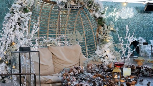 A christmas alcove with a wicker bench covered in snowy decorations next to lanterns at the lucky club rooftop in london.