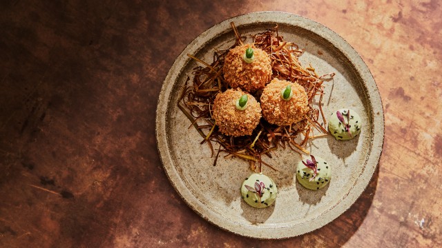 Trois croquettes de pommes de terre disposées avec art dans une assiette sur une table en bois.