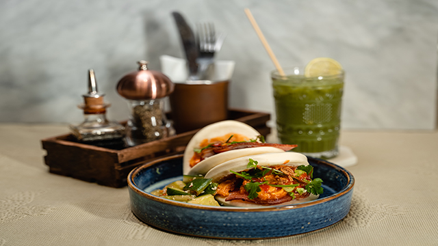 A plate of warm and fluffy bao buns, filled with crispy onions and smacked cucumbers.