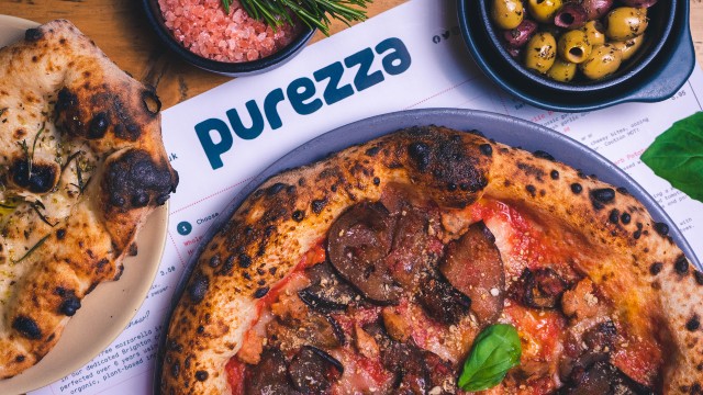 Vegan pizza, olives and pizza bread laid out on a table featuring a Purezza restaurant menu.