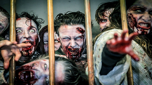 A group of zombies at a london immersive experience try to grab visitors through the bars.