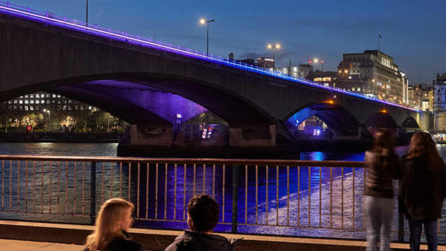 People looking at the illuminated bridge on the river Thames in the evening